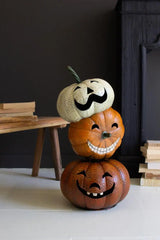 3 stacked jack-o-lanterns with different smiles and grins - sitting on the floor next to a black mantle