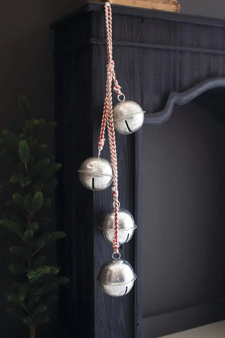 4 silver bells on red and white braided string hanging from a black mantel