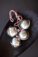 4 silver bells on red and white braided string in a dark metal bowl