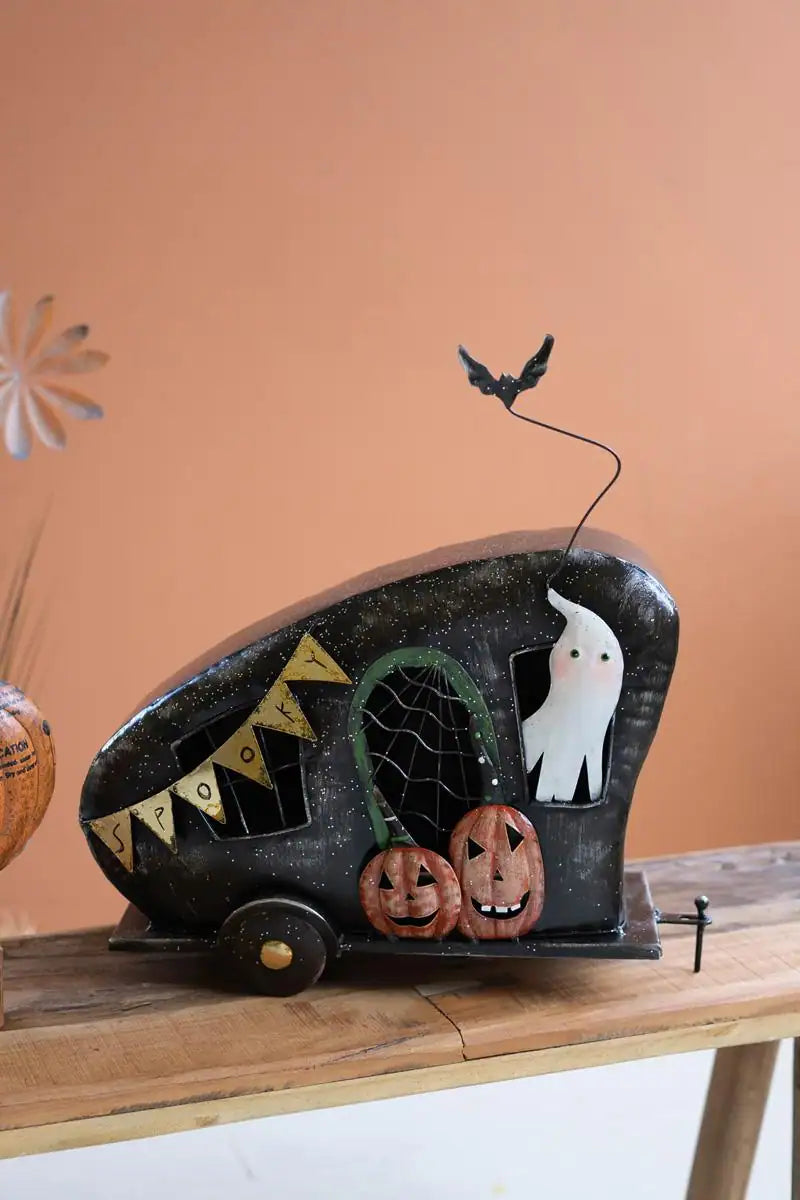 halloween themed metal camper with spider web covering the door with pumpkins on the baseboard a ghost coming out of the window and a bat atop