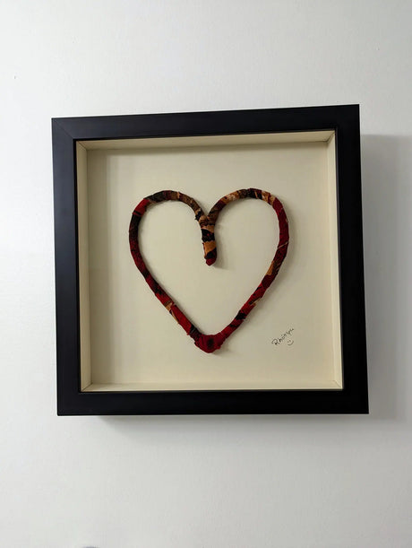 multicolored recycled fabric heart in black wood frame behind museum glass
