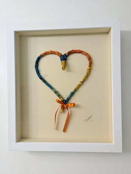 multi-colored recycled fabric heart in white wood frame behind museum glass