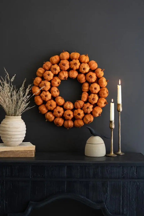 faux orange pumpkin wreath - shown hanging on dark gray wall with 2 burning candles and black mantle fireplace