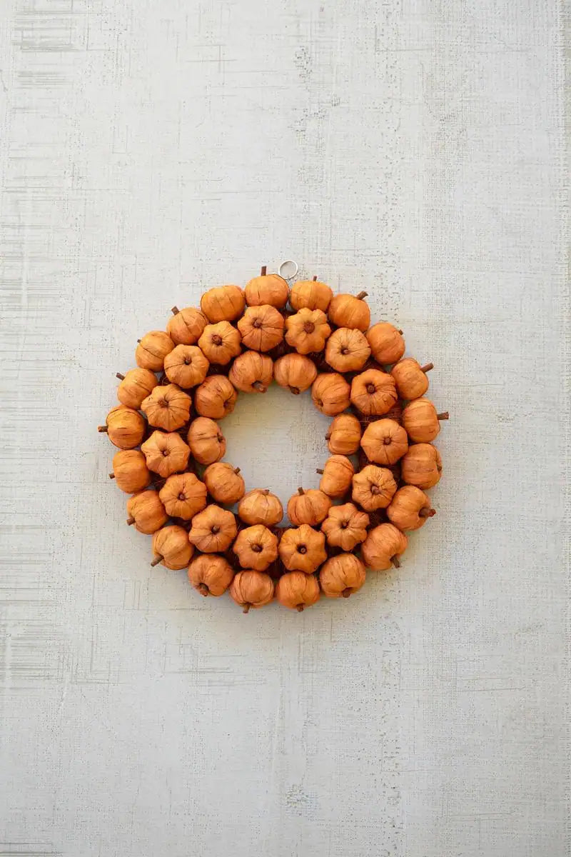 artificial orange pumpkin wreath on slightly textured white background