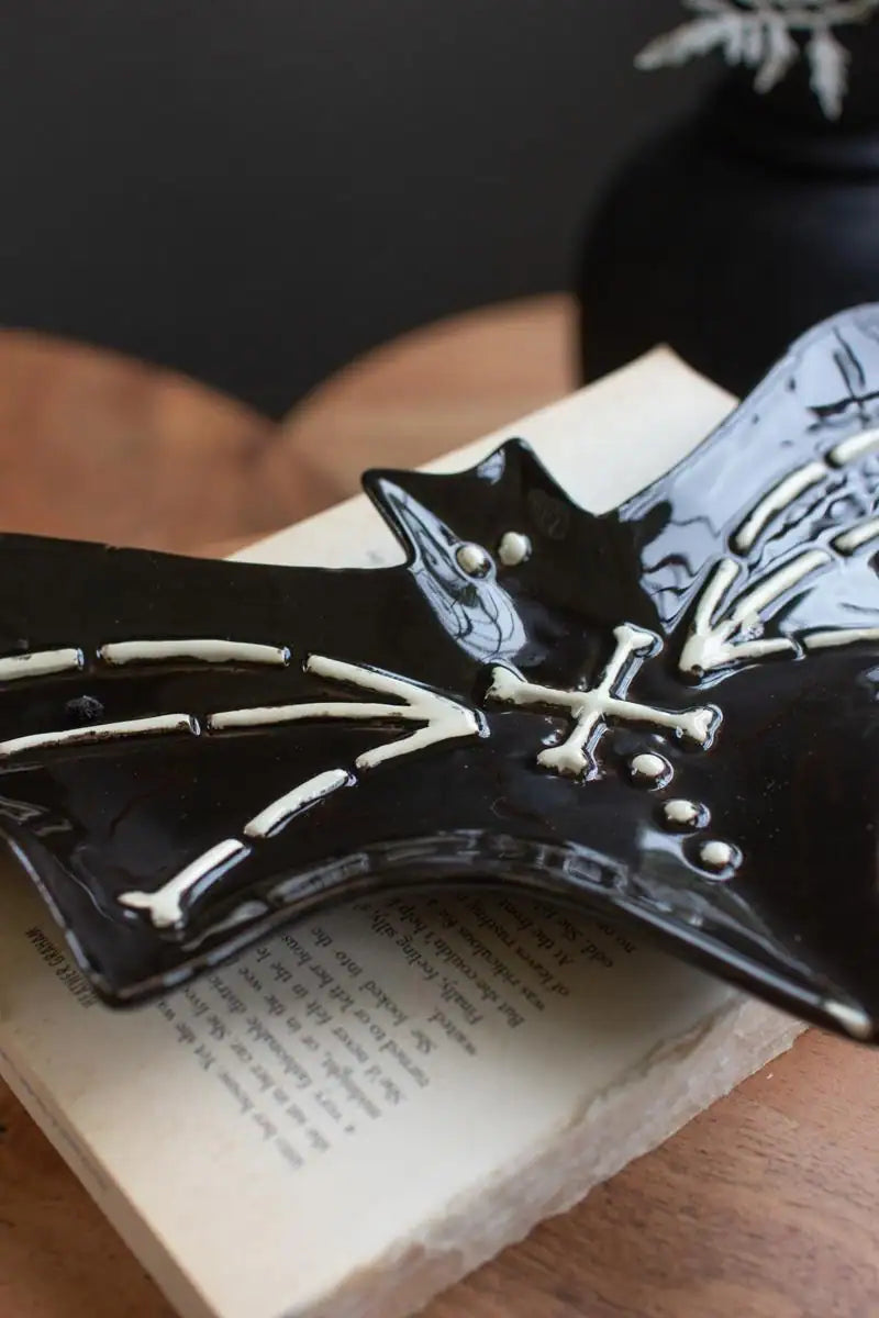 2 black ceramic bat platters with white bones detail - angled close up of bat platter sitting on old book