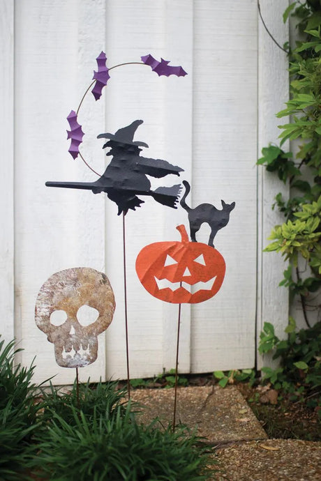 flying witch and bats, black cat on an orange pumpkin and skeleton head yard stakes against white fence background