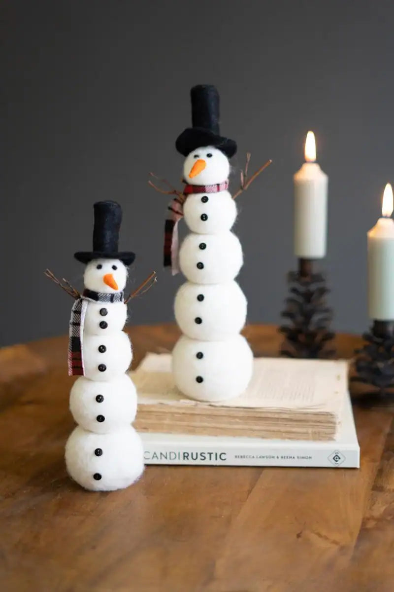 2 felt snowmen one atop some books with lit candles in the background