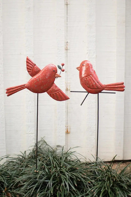 2 red birds on yard stakes - one carrying mistletoe toward the other