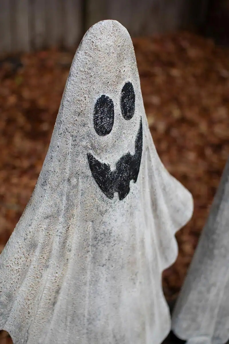 2 white ghosts - both smiling - the tall one has 4 teeth - the small one has black smile - angled view of toothy ghost head