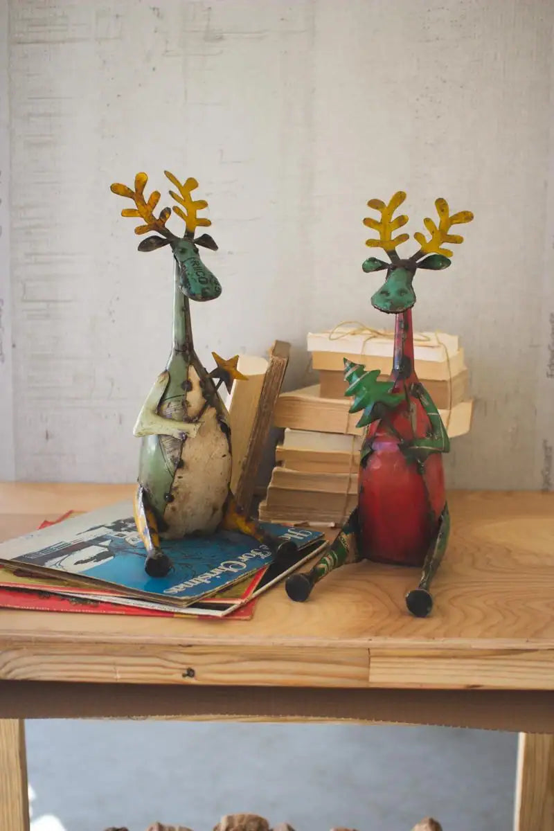 2 metal deer sitting on a shelf - one green holding a star wand the other red holding a christmas tree wand