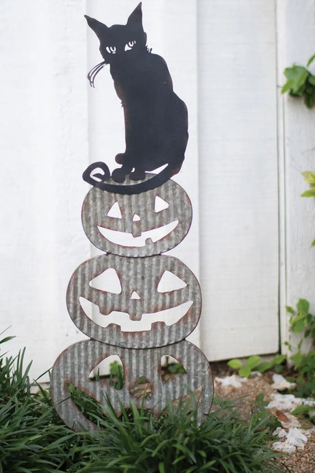 jack-o-lantern of 3 pumpkins with black cat on top showing its mischievous eyes - white fence background