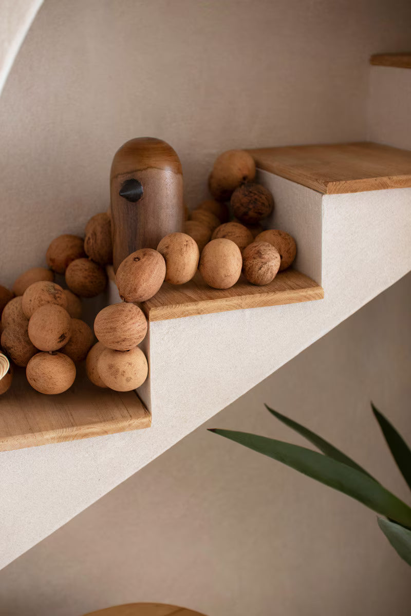Wood covered stair detail in top of shelf with large wood beads on a neutral background