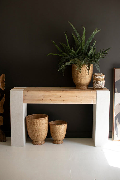 Wooden console table with decorative plants and vases against a dark wall.