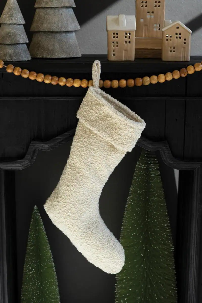 white boucle fabric christmas stocking hanging from black mantel under other christmas décor