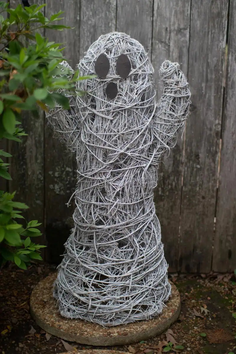 white twig ghost with its arms up - standing in front of faded wooden fence