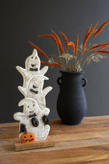 white wood ghosts stacked and smiling at the viewer with an orange pumpkin at the base