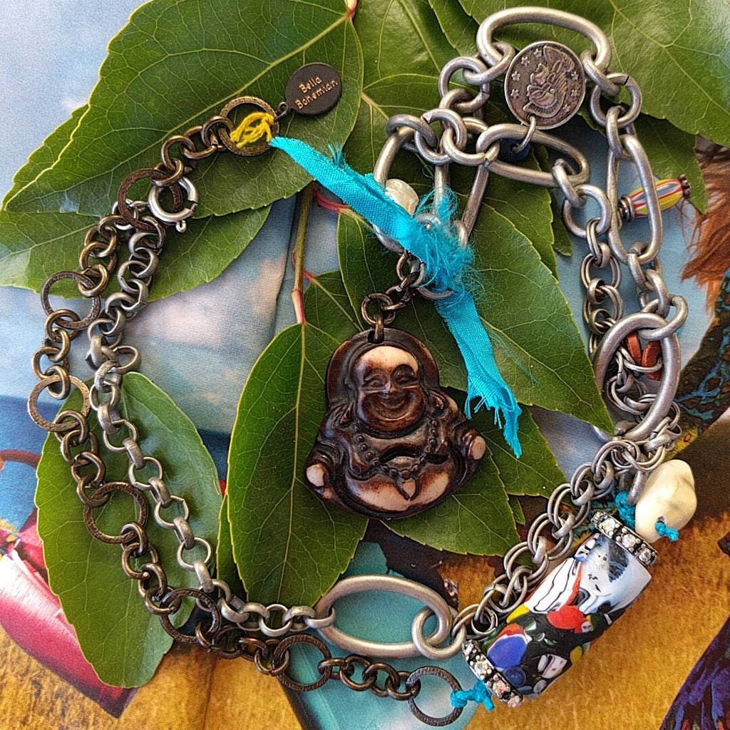 handmade mixed-metal necklace with hand carved happy buddha sitting on some green leaves
