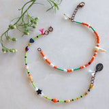set of 2 handmade bracelets with white, creme and orange glass beads, tiny dark blue heart and tiny black star, lemon green skinny tube, pink tassel