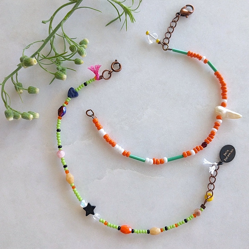 set of 2 handmade bracelets with white, creme and orange glass beads, tiny dark blue heart and tiny black star, lemon green skinny tube, pink tassel