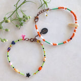 set of 2 handmade bracelets with white, creme and orange glass beads, tiny dark blue heart and tiny black star, lemon green skinny tube, pink tassel