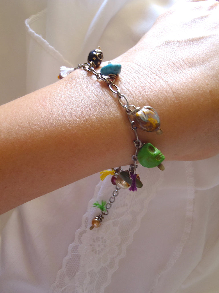 charm bracelet with peacock, burgundy fresh water pearls, jade bear, and green skull shown on a lady's wrist