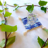 single square boho royal blue and ivory colored heavy linen coaster with filled drink - side view