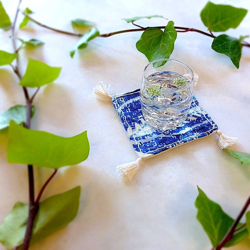 single square boho royal blue and ivory colored heavy linen coaster with filled drink - side view
