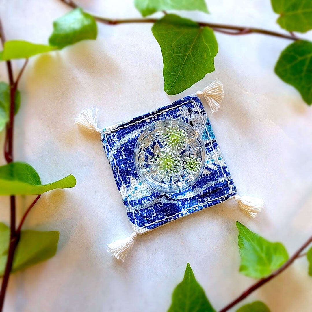 single square boho royal blue and ivory colored heavy linen coaster with filled drink - top down view