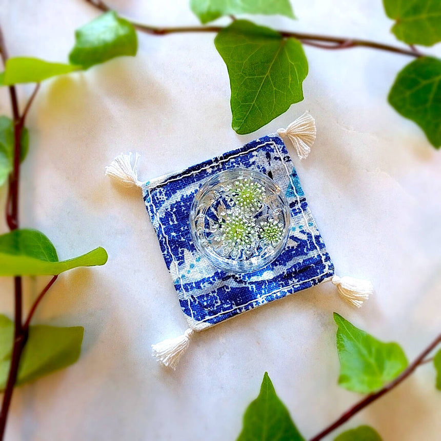 single square boho royal blue and ivory colored heavy linen coaster with filled drink - top down view