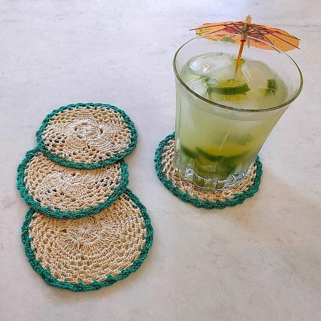 set of four round crochet cotton yarn coasters in natural tan color and teal border - shown with umbrella drink