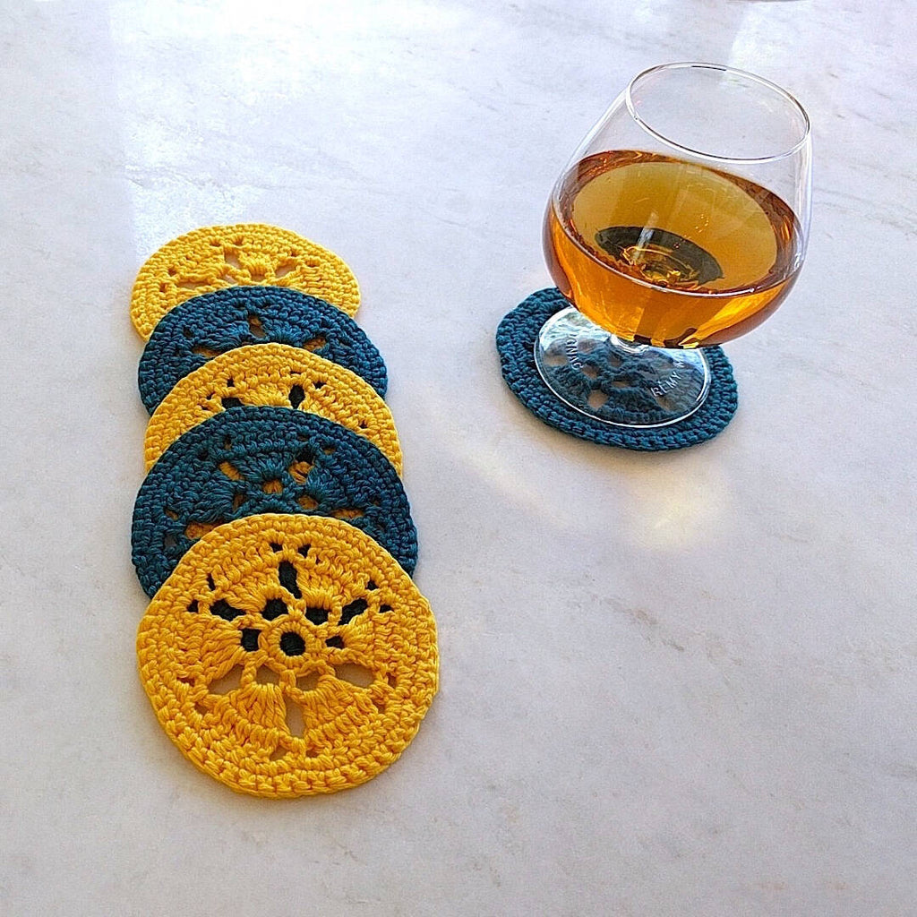 two bright yellow and two earth dark green crocheted coasters shown with a glass of cognac