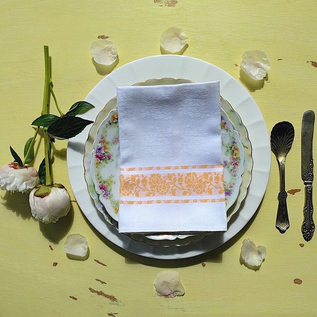 set of four square white cotton napkins with orange detail and flower pattern