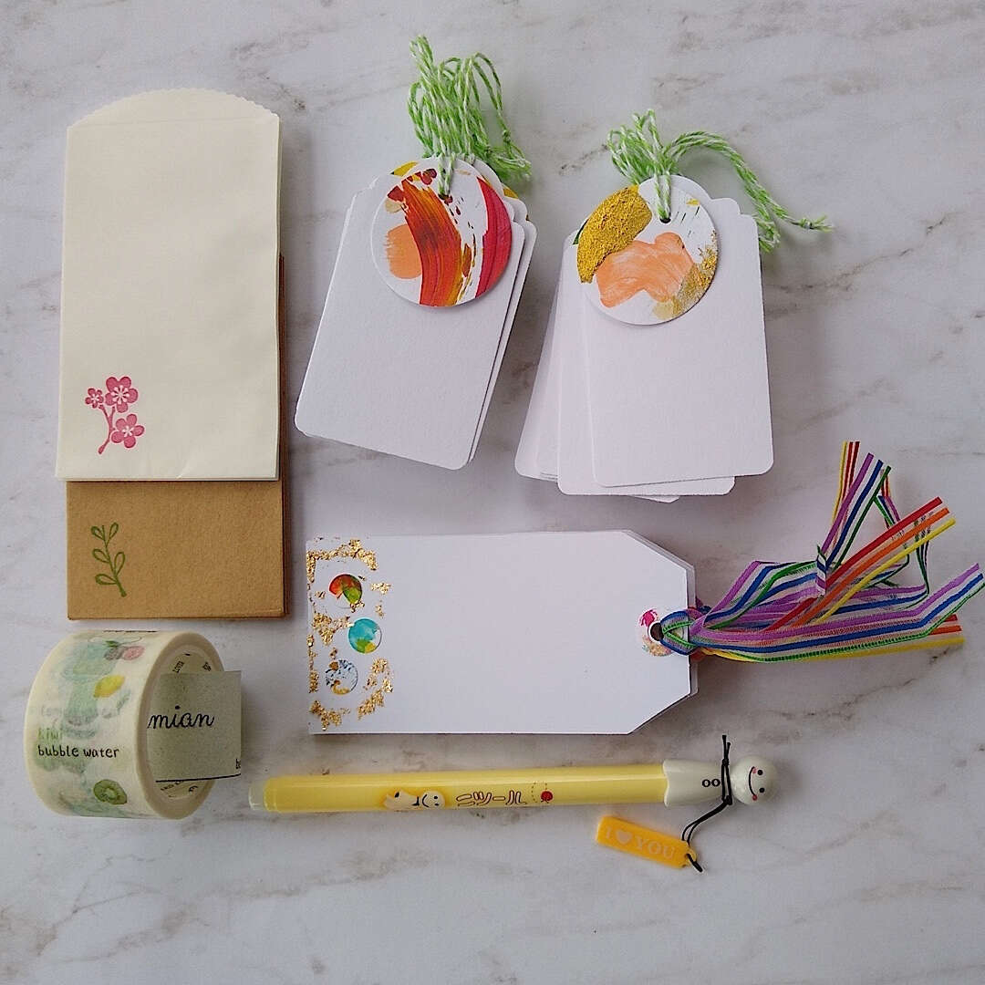 confetti and gold foil gift cards, white gift tags, mini envelopes, Japanese washi tape, Japanese sunny doll black pen laid out differently on a table