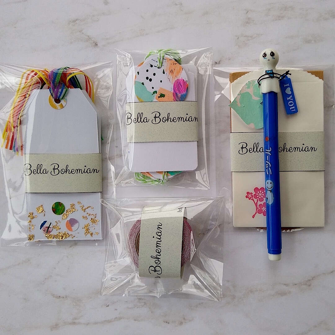 abstract confetti and gold foil gift tags, white gift tags, mini envelopes, Japanese doll pen, Japanese washi tape, plastic wrapped laid out on a table ready to pack