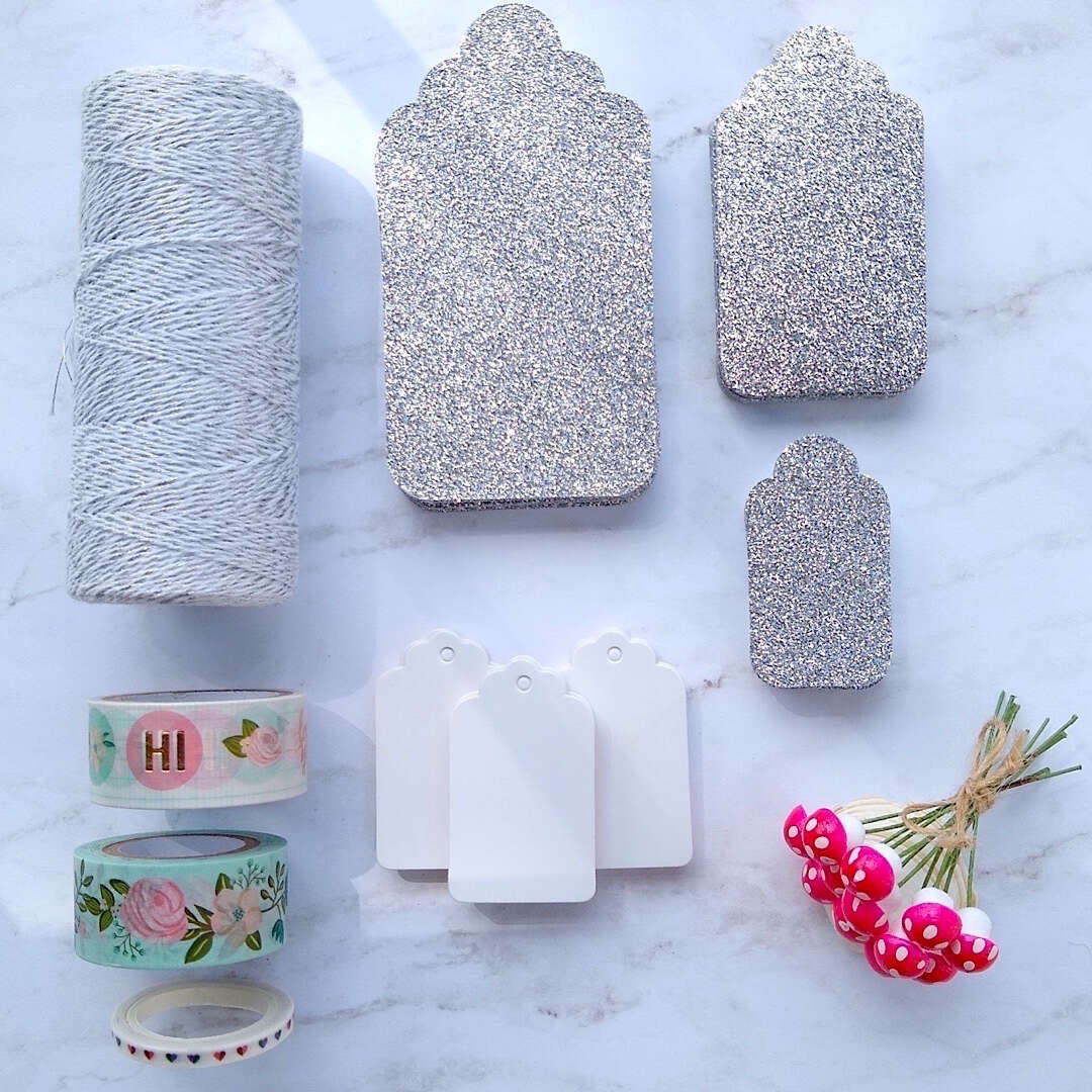 silver luxe glitter gift cards, white hang tags, German cotton spun mushrooms, metallic glitter bakers twine laid out flat
