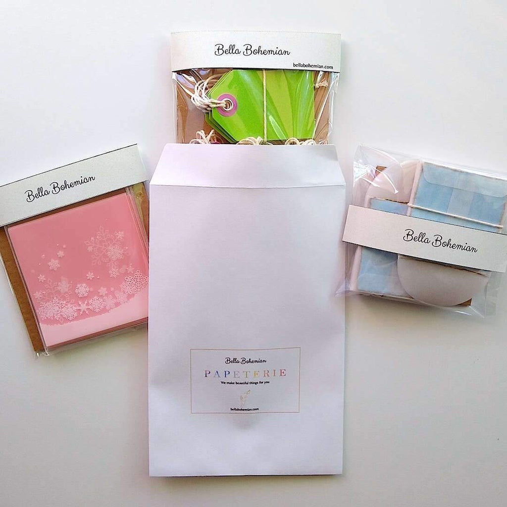 3 wrapped papeterie packs including gift tags, snowflakes favor bags, watercolor cards and glassine envelopes shown with Bella Bohemian branded envelope